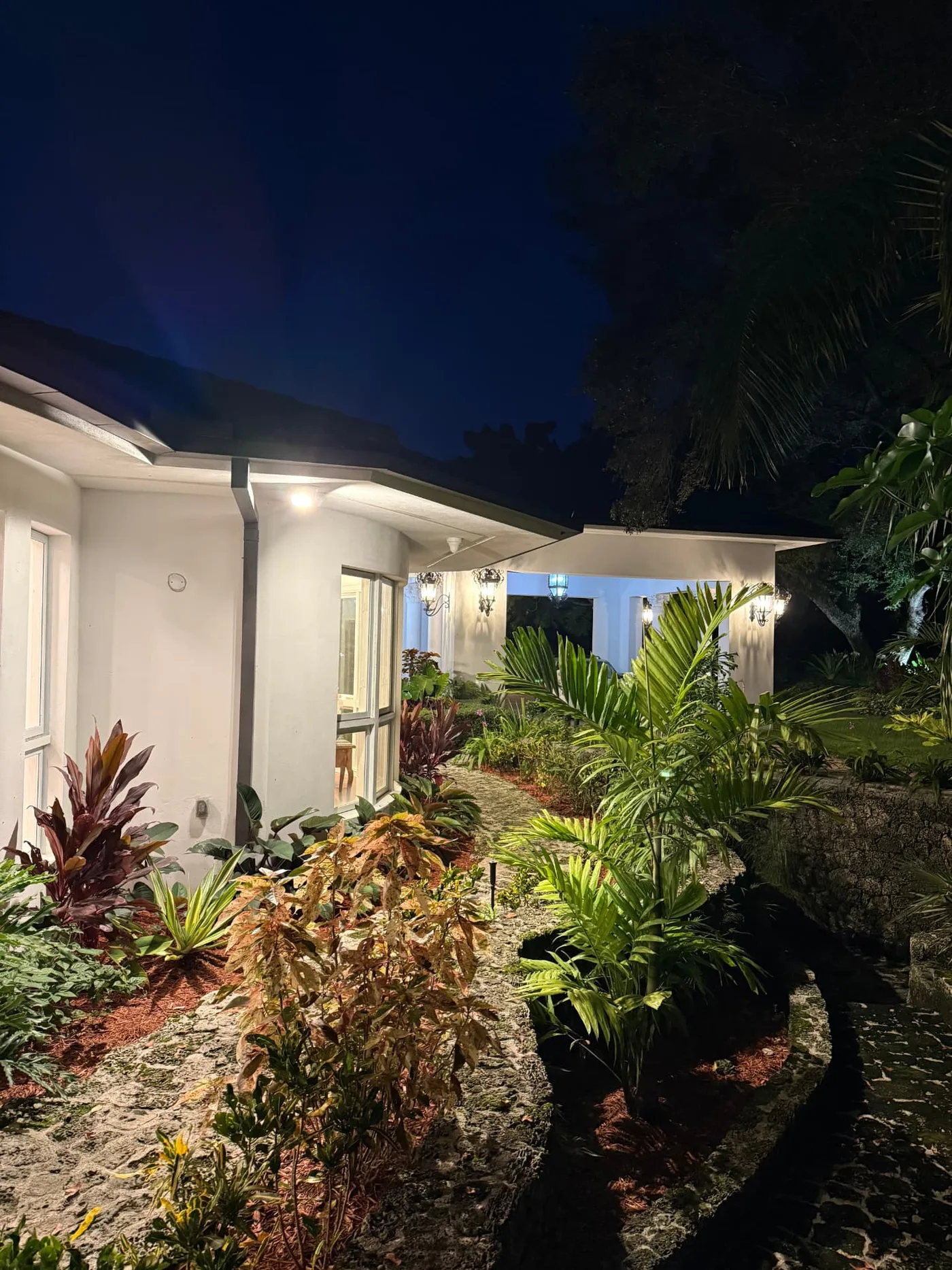 Entrada de casa con plantas y jardín iluminados de noche, trabajo de ARAC Electric