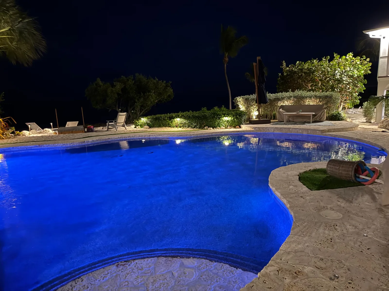 Piscina con iluminación azul y jardín iluminado de noche, trabajo de ARAC Electric